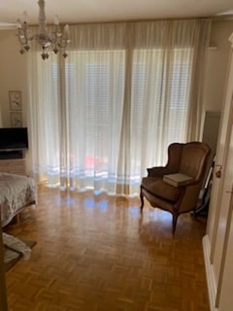 A room with wooden floors, a bed, a chair, a television, and a chandelier.