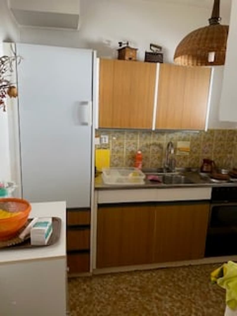 A kitchen with wooden cabinets, a white refrigerator, a sink with a faucet, and a tiled floor.