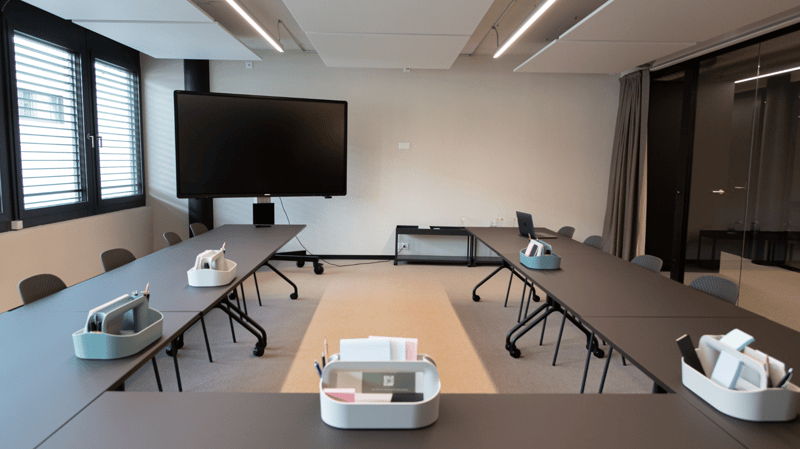 Empty conference room with a table, chairs, long tables, monitors, and a large screen at the front.