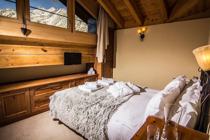 a large bed in the center, wooden shelves on the side, TV mounted on the wall, a lamp, mountains view through the windows