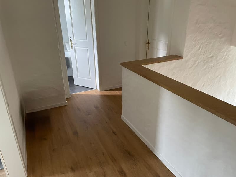 Empty room with white walls, wooden floor, and a white door.