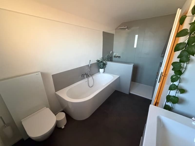 Bathroom with bathtub, toilet, and shower stall. Grey tiled walls and white fixtures.