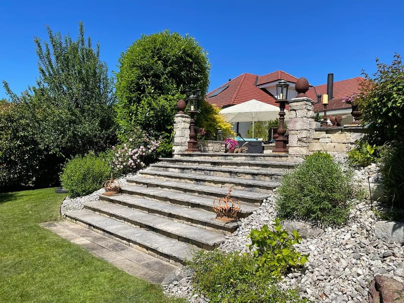 stone steps with railings, stone walls, garden area with shrubs and flowers, house in the background