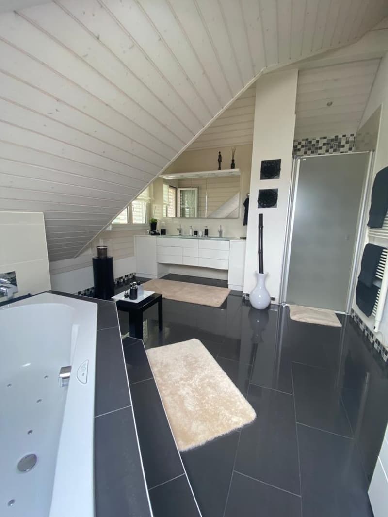 modern bathroom with white bathtub, black and white tiled floor, white countertops, ceiling with beams, mirror and shower