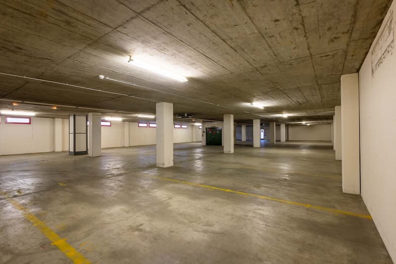 Large open parking garage with concrete floor, exposed ceiling, and yellow parking lines on the floor.