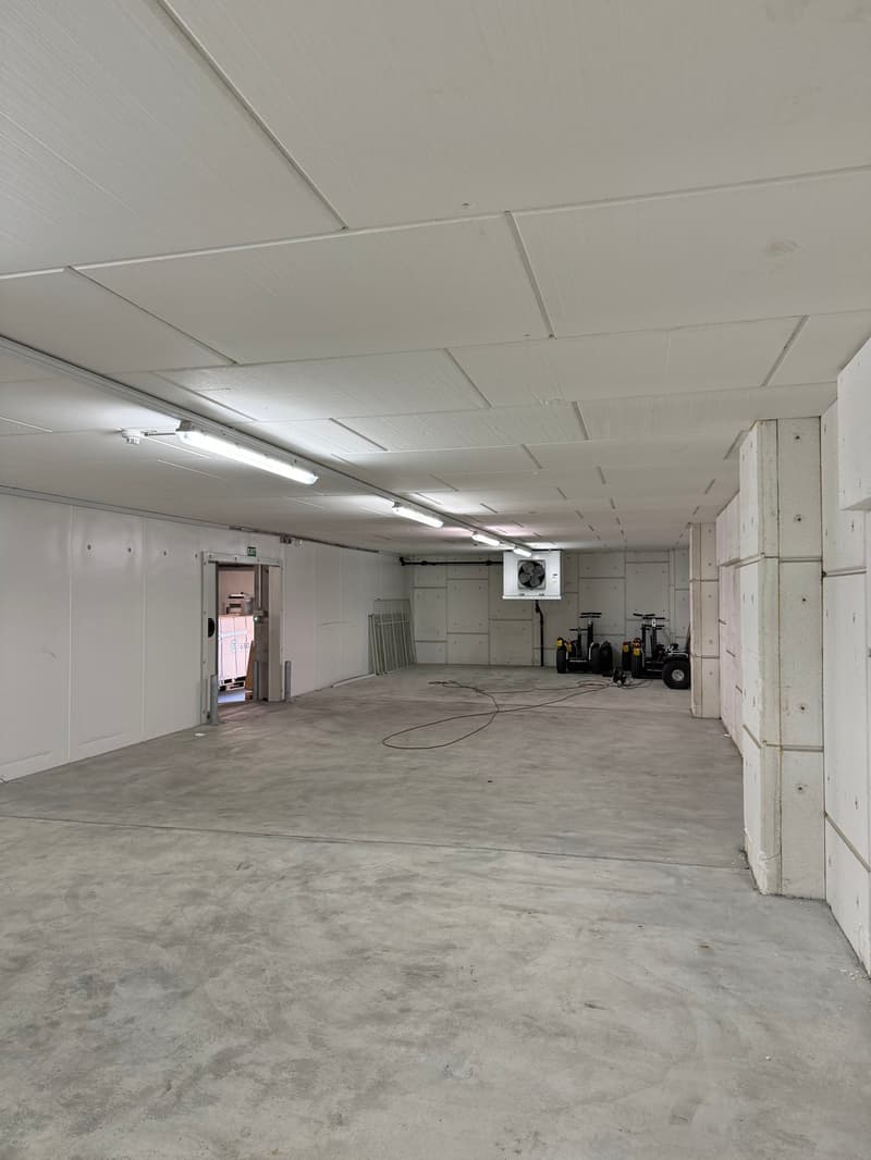 Empty room with white walls, concrete floor, mounted lights, and an air conditioner unit.