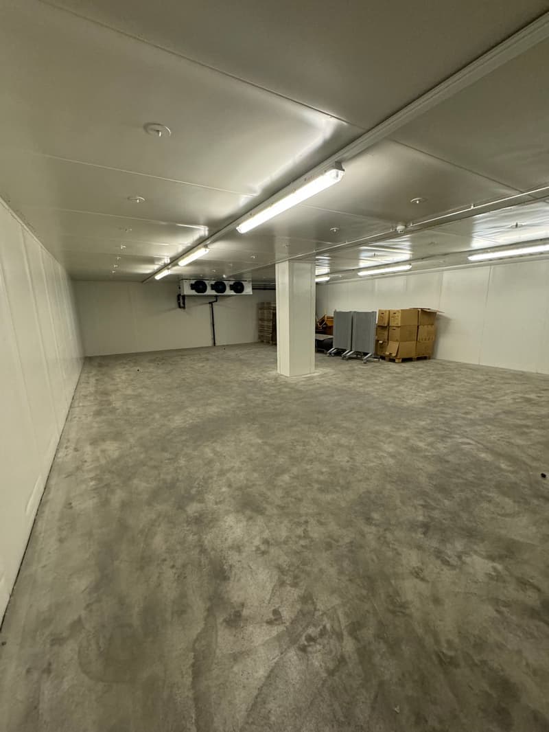 Empty room with concrete floor, white walls, and multiple lighting fixtures, some AC units, and storage boxes.