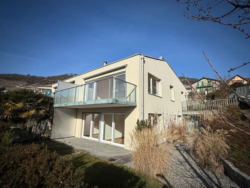 Modern house with two floors, glass balcony, glass doors, beige facade, concrete walkway, trees and plants