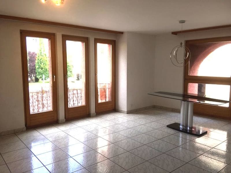 Large room with balcony, white tiled floor, glass table, arched windows