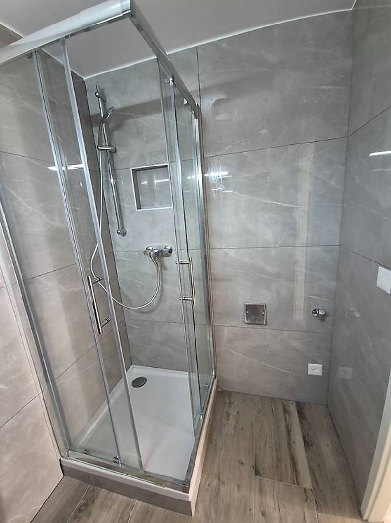 Modern and stylish glass walk-in shower with wooden flooring, wall-mounted shower head, shower arm, and shower head with a flexible hose