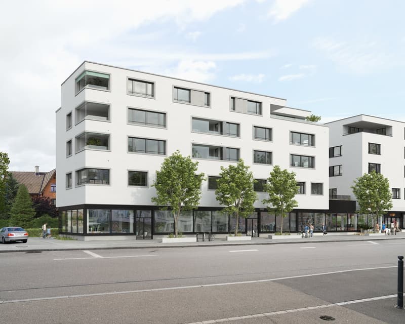 Modern white building with multiple windows, ground floor commercial space, trees in front, paved road, people walking