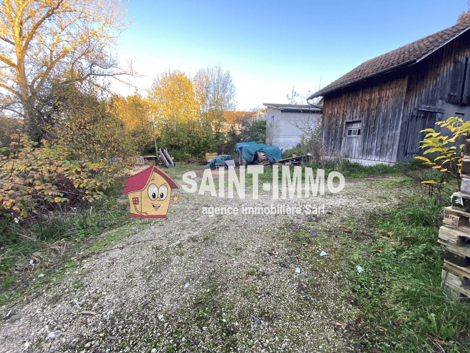 Wooden barn or shed, gravel path, trees with autumn foliage, outdoor equipment or storage