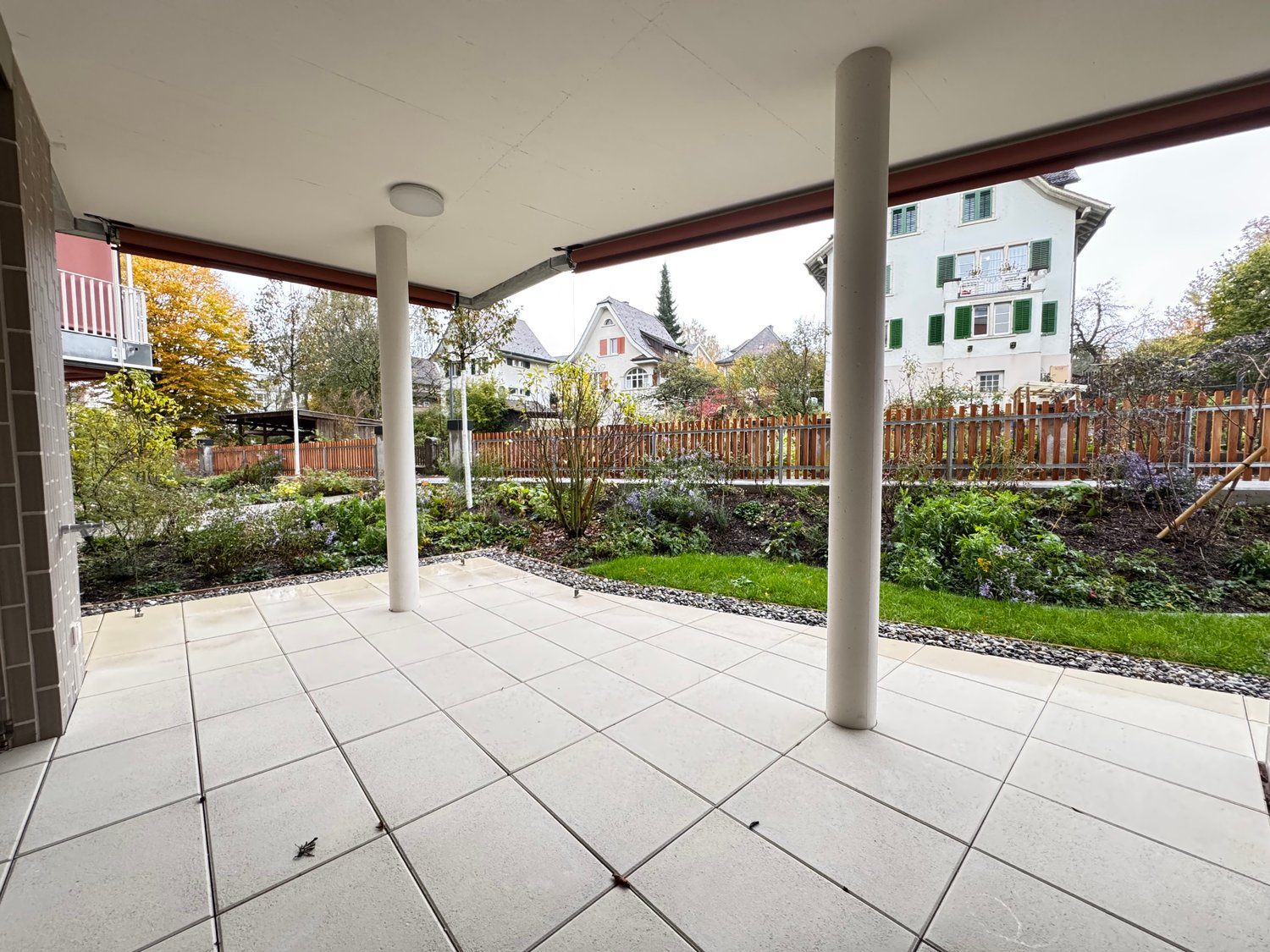 covered area, tiled flooring, white tiles, white pillars, wooden fence, well-maintained garden, plants and trees