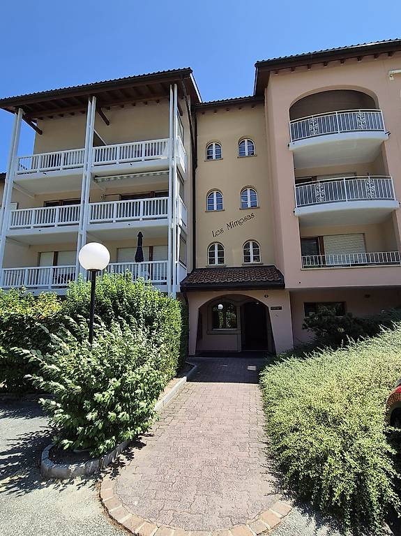 A two-story apartment building with several balconies, white railings, and a brick walkway.