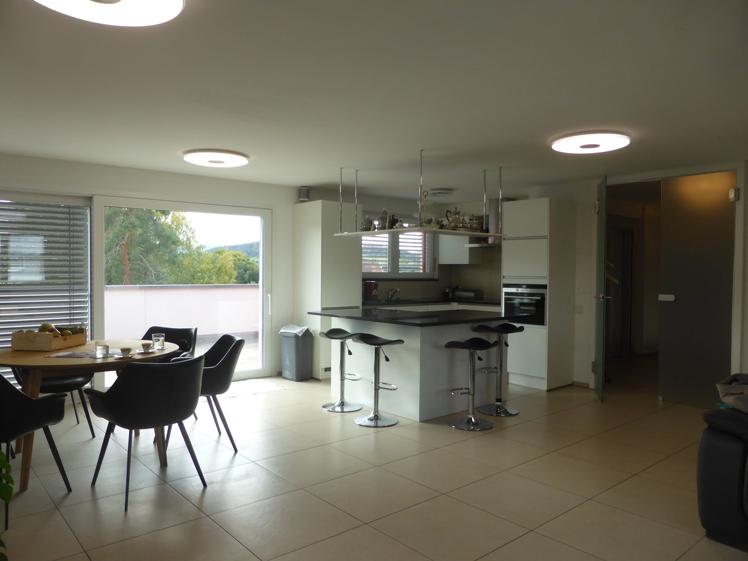 open plan kitchen and living room, modern decor, white tile flooring, balcony with terrace, large windows with view