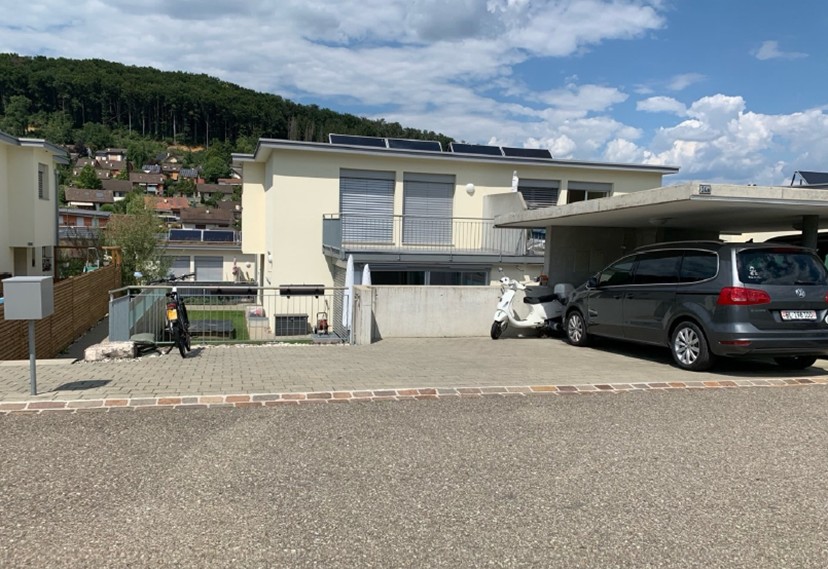white house, concrete garage, cars parked, solar panels on the roof, fenced yard, mountains in the background