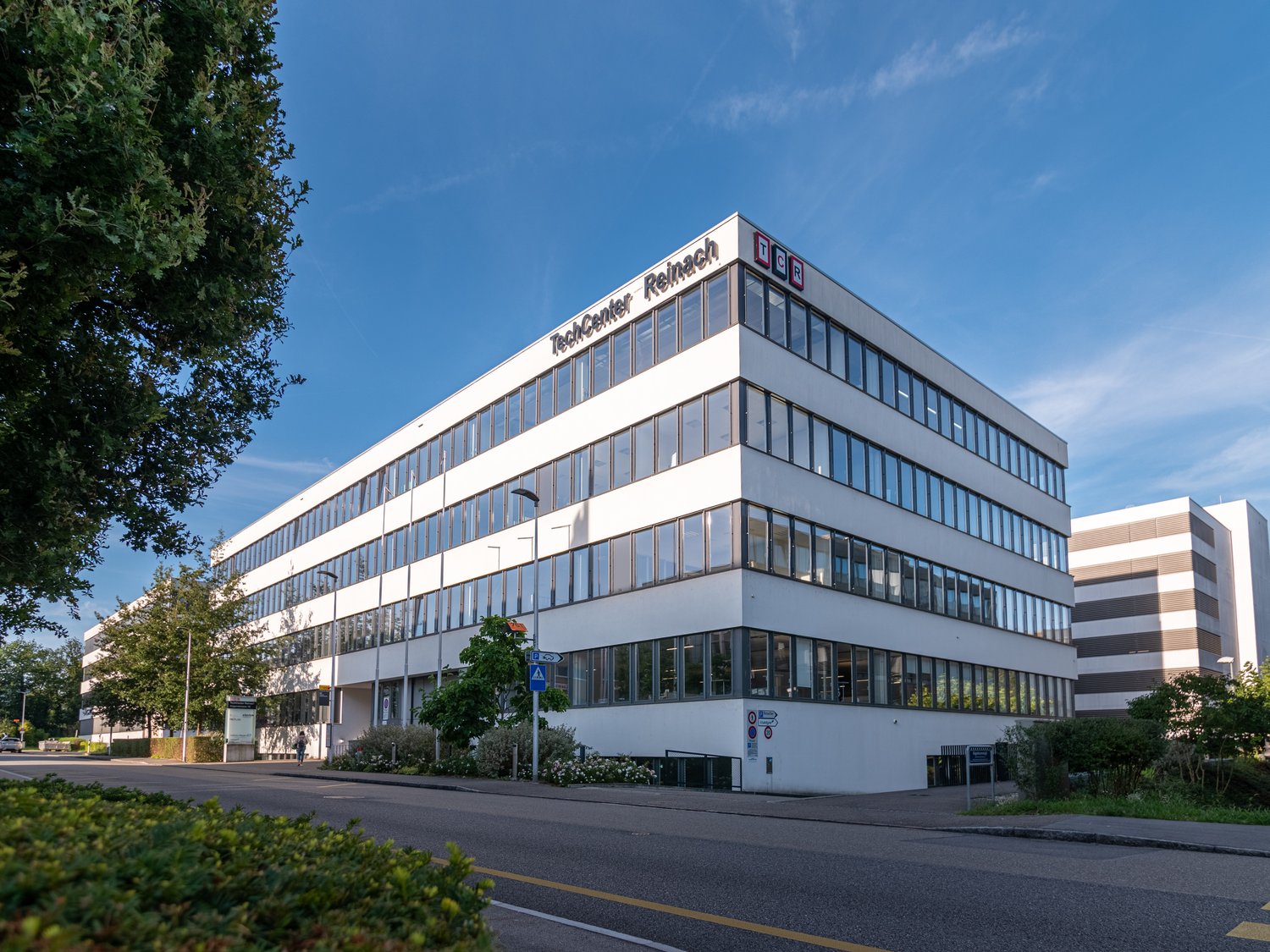 TechCenter Reimach is a 4 story white office building with glass windows, located on the side of the road