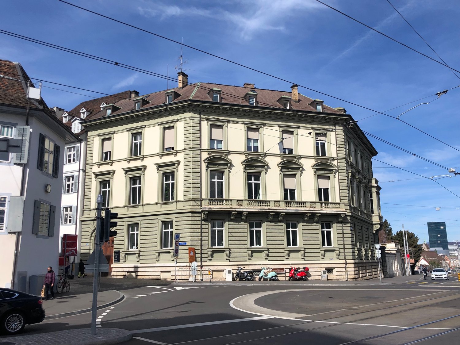 corner building, multiple stories, green color, balcony, windows, traffic lights, people, motorcycles