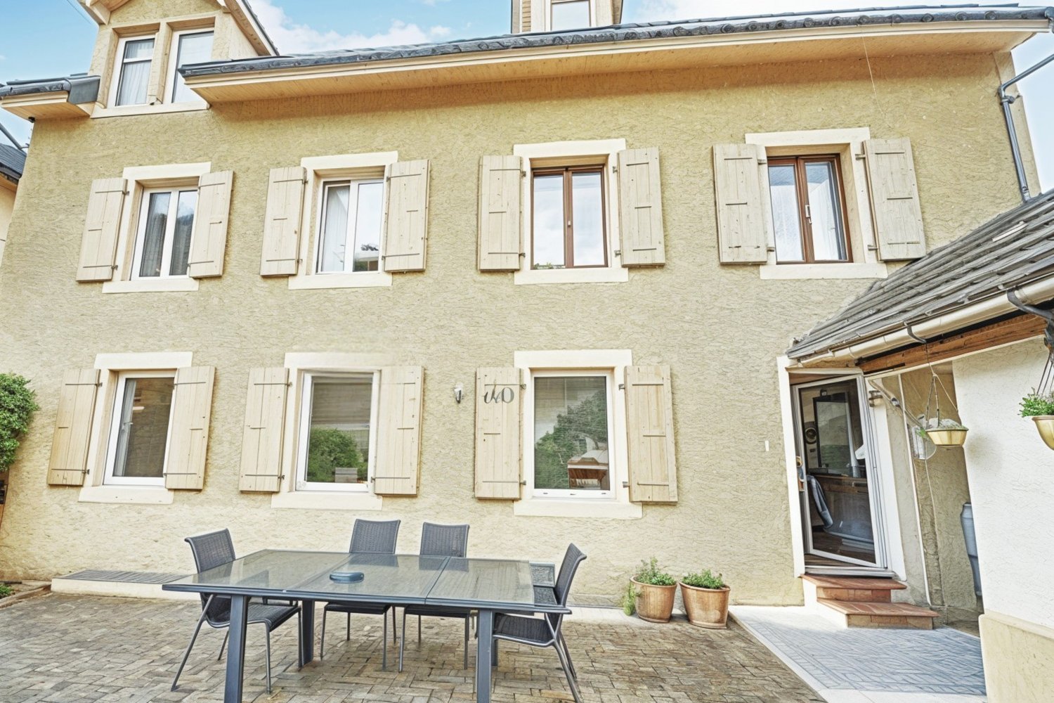 2 story house, beige exterior, white shutters, glass table, chairs, potted plants, entrance