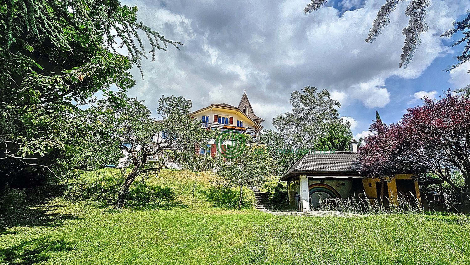 House on a hill, surrounded by trees, spacious lawn, small wooden house, steep stairs, white exterior, red trims