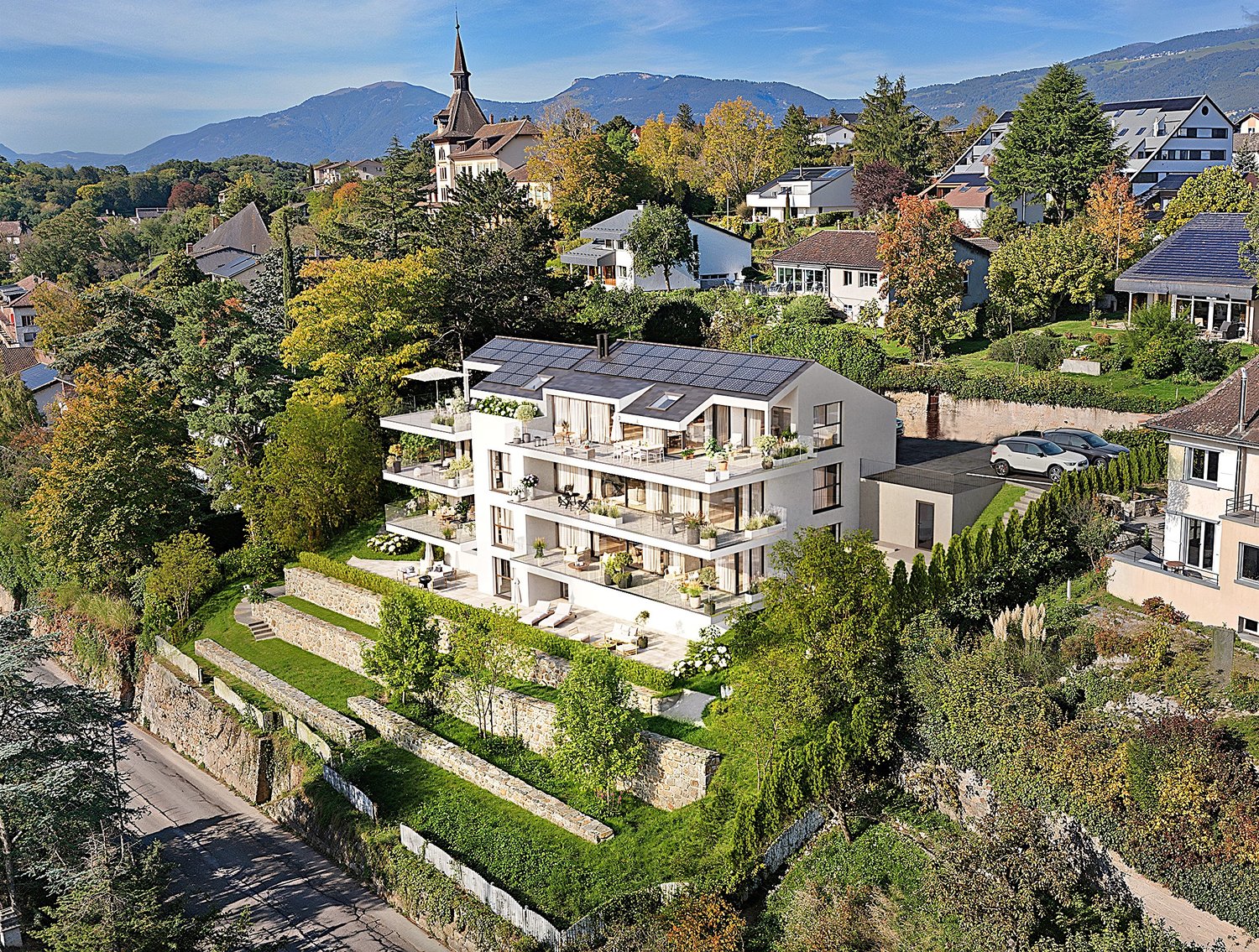 Modern white house with solar panels, multiple balconies, surrounded by trees and greenery, with a view of the mountains