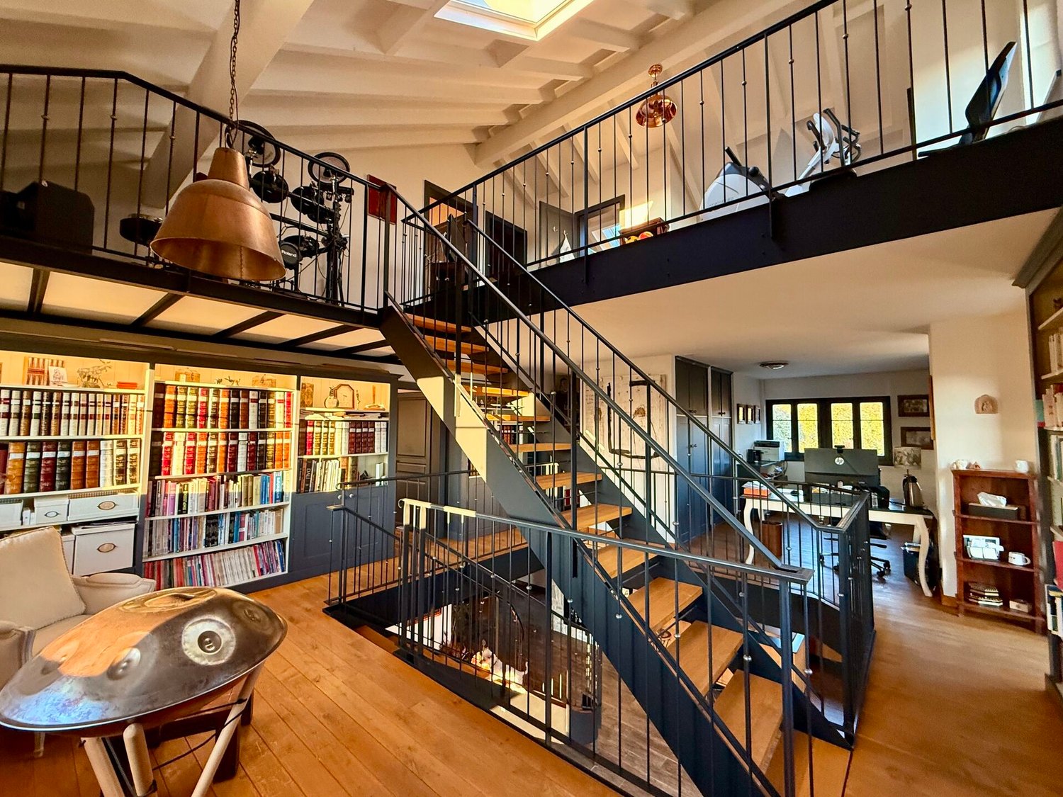 High ceiling, wooden floor, spiral staircase, study with bookshelves, living room with couch, musical instrument, balcony with drum set
