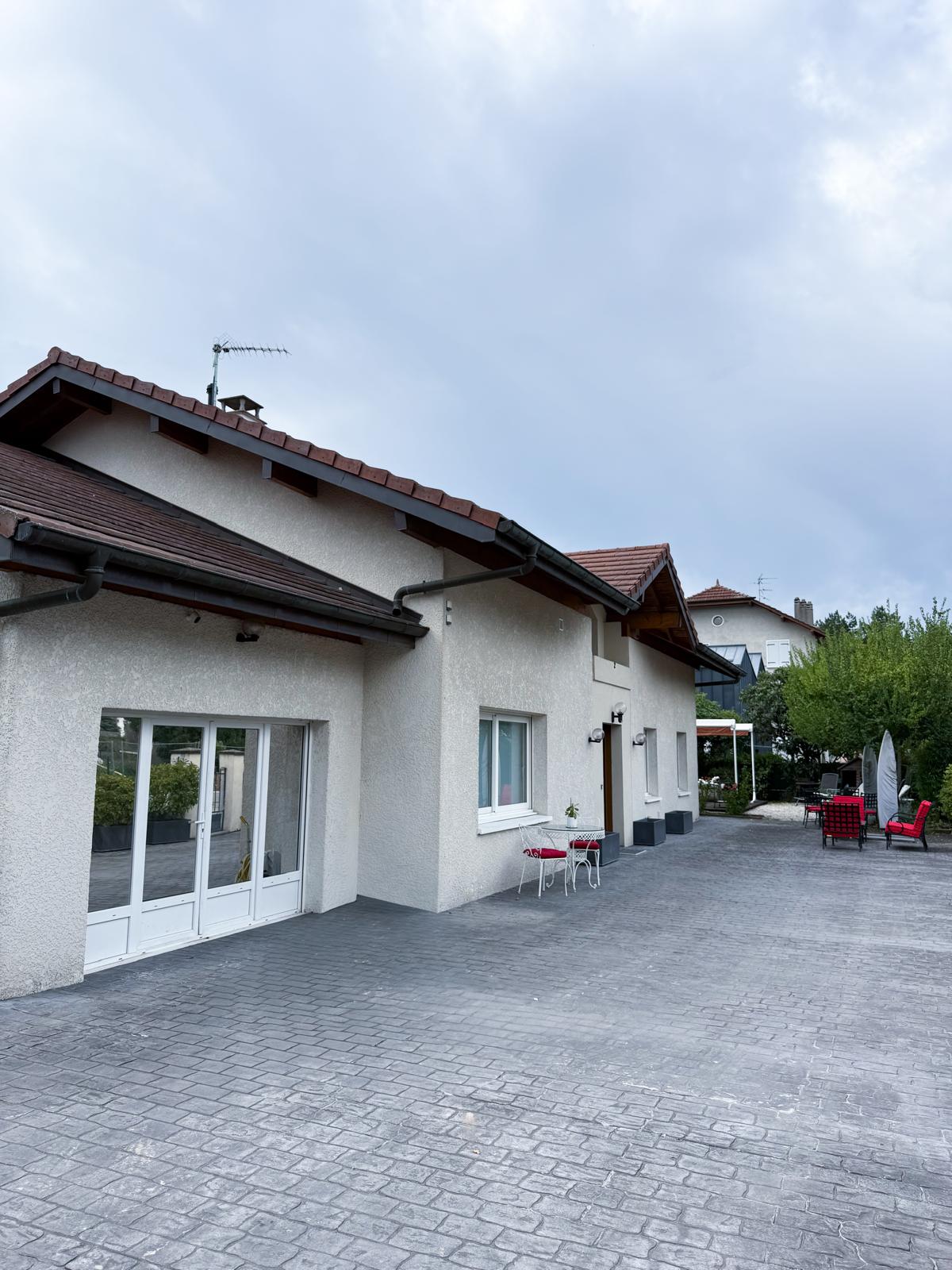 Detached house, white exterior, tiled roof, double glass doors, small table with chairs, outdoor seating area, paved driveway