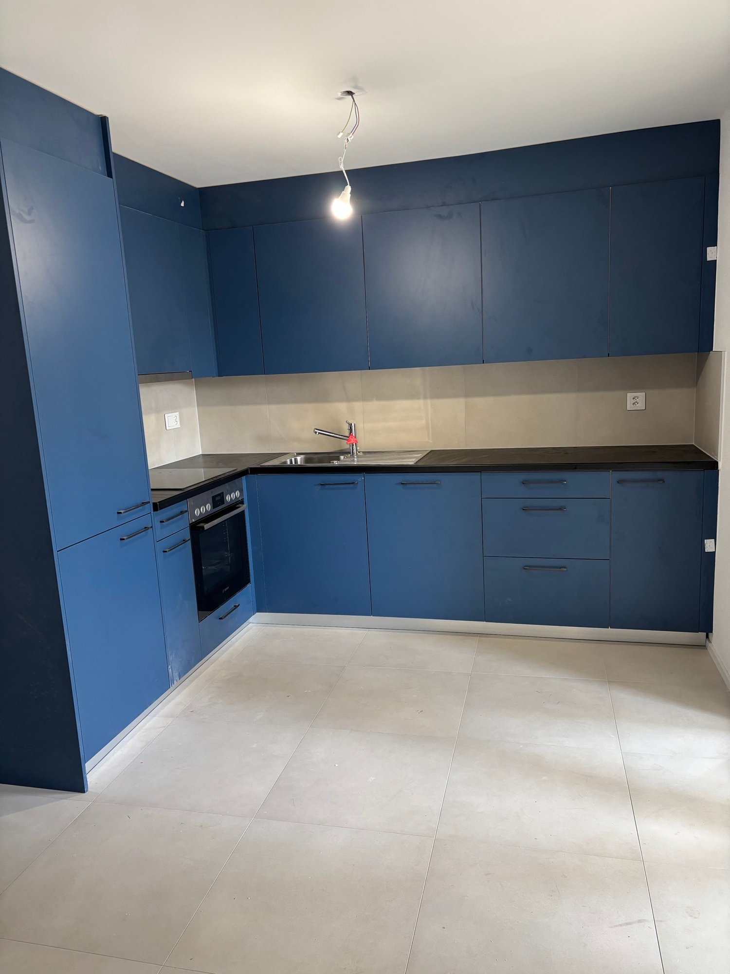 modern kitchen, blue cabinets, tile floor, black countertops, integrated oven, silver sink and faucet, overhead light