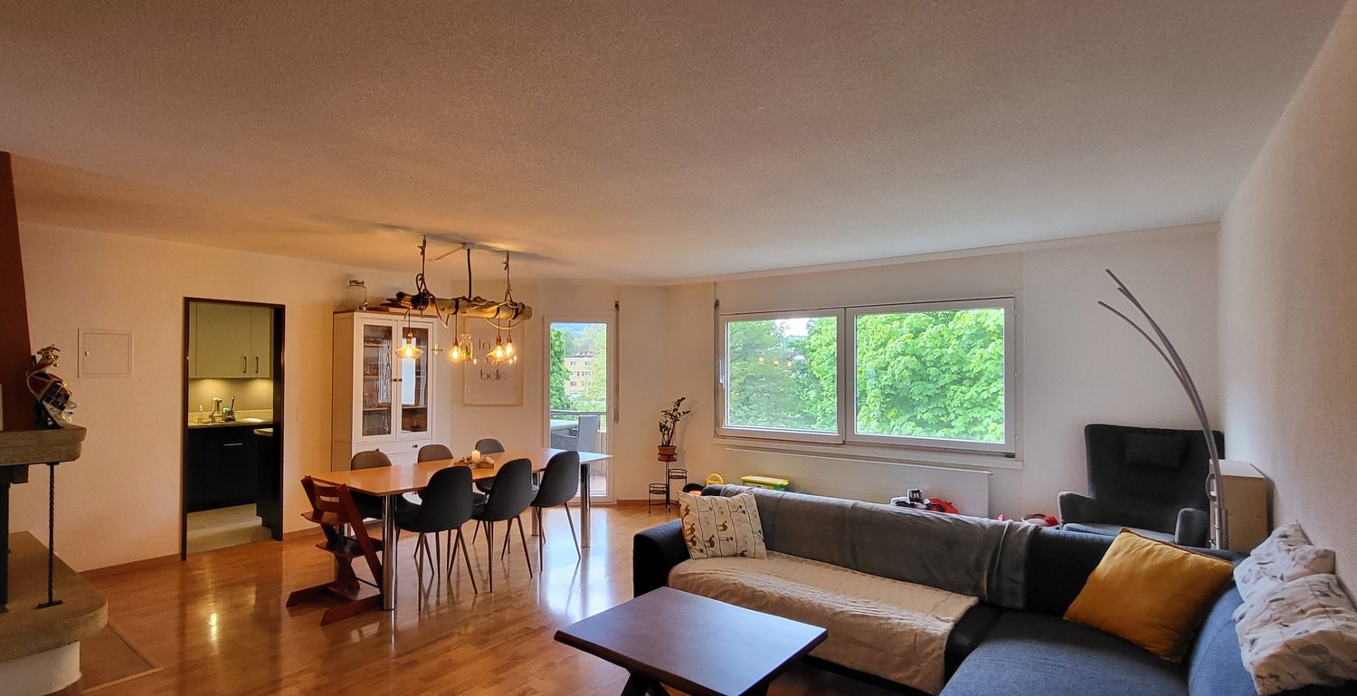 Living room with dining area, wooden floor, fireplace, sofa, coffee table, chandelier, dining table with chairs, window with view