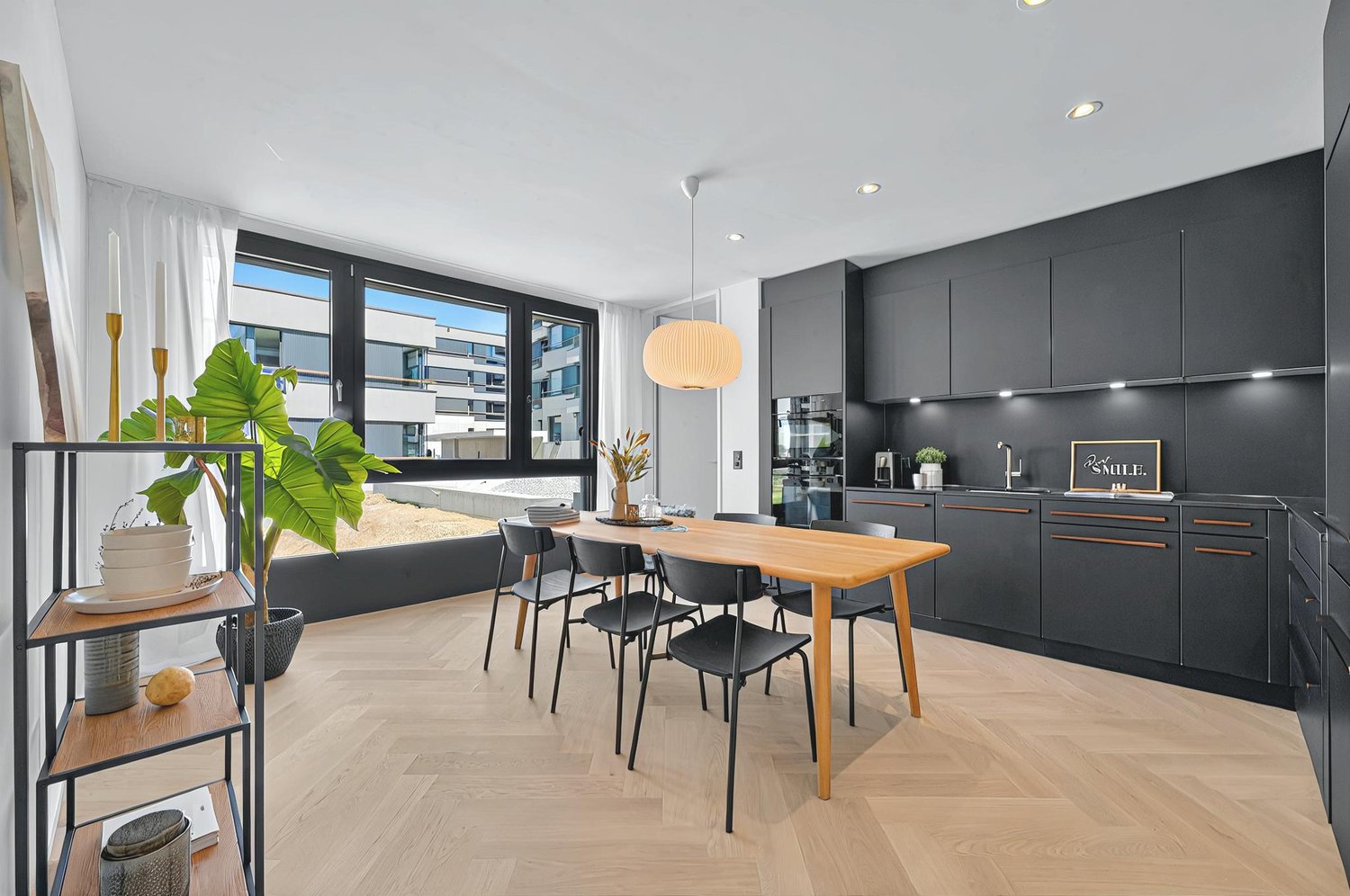 dining area with wooden table, black chairs, kitchen with black cabinets, kitchen island, plant, view of outside