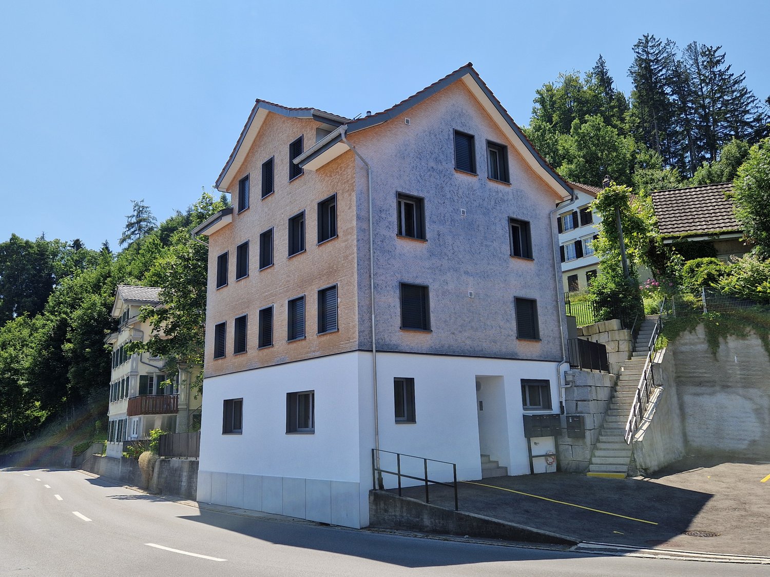 3 story house, brown and white exterior, multiple windows, located on a slope, surrounded by trees