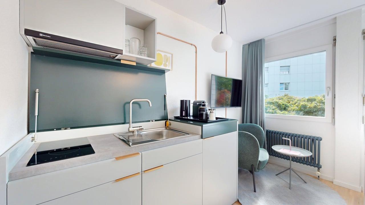Open plan kitchen, gas stove, stainless steel sink, extractor fan, television, chairs, radiator, windows