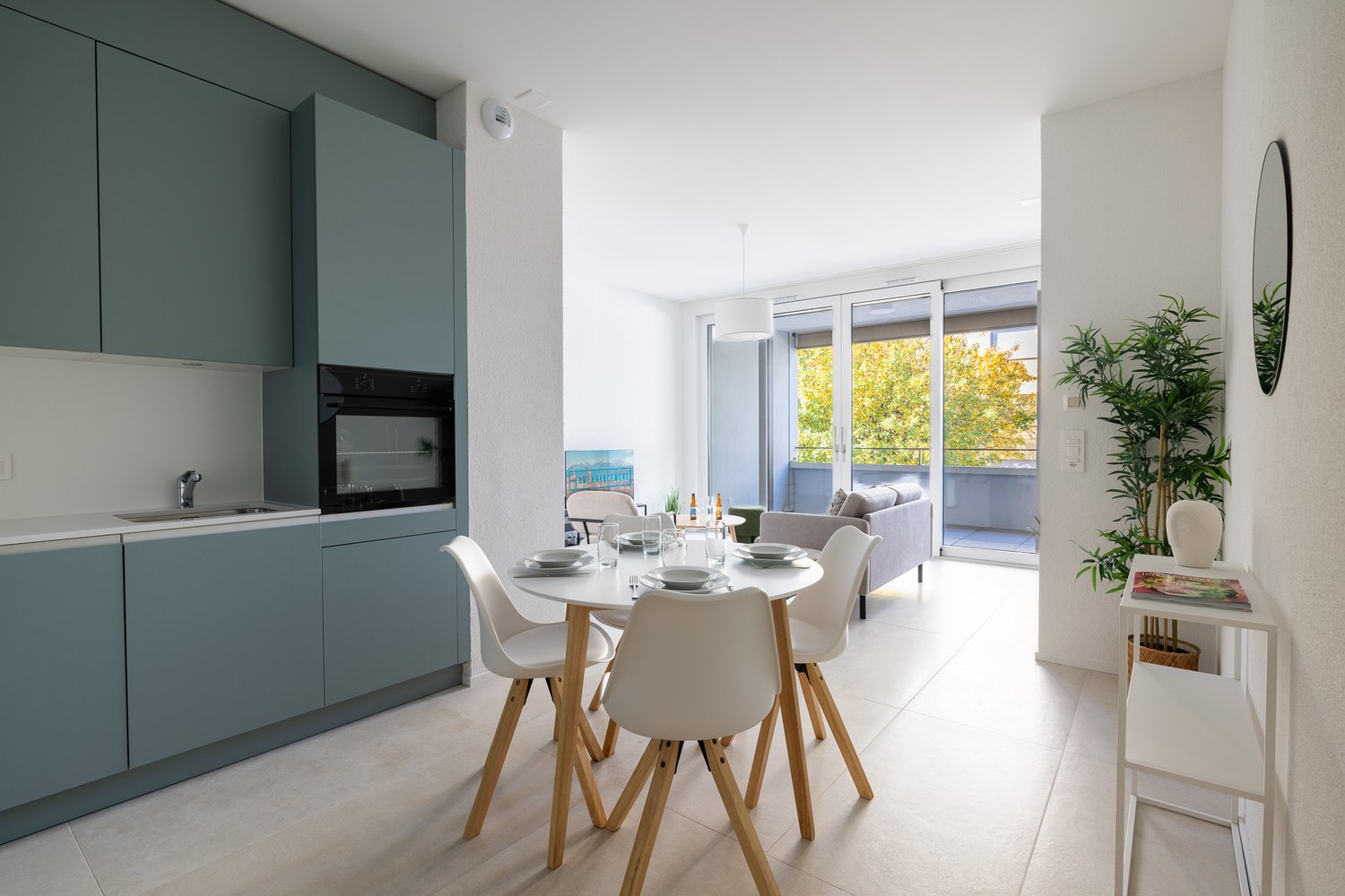 modern kitchen with dining area, white cabinets, white countertops, modern appliances, dining table, chairs, balcony with couch, potted plant