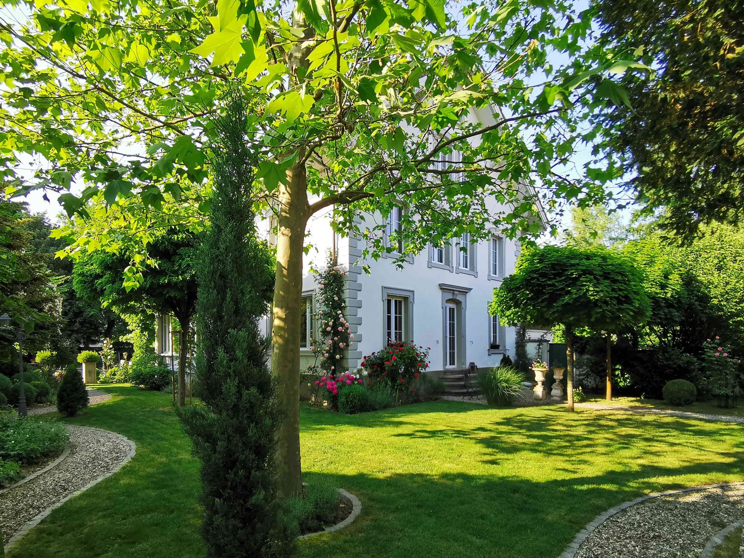 2 story house, white exterior, surrounded by green lawn, flower garden, trees, pathway