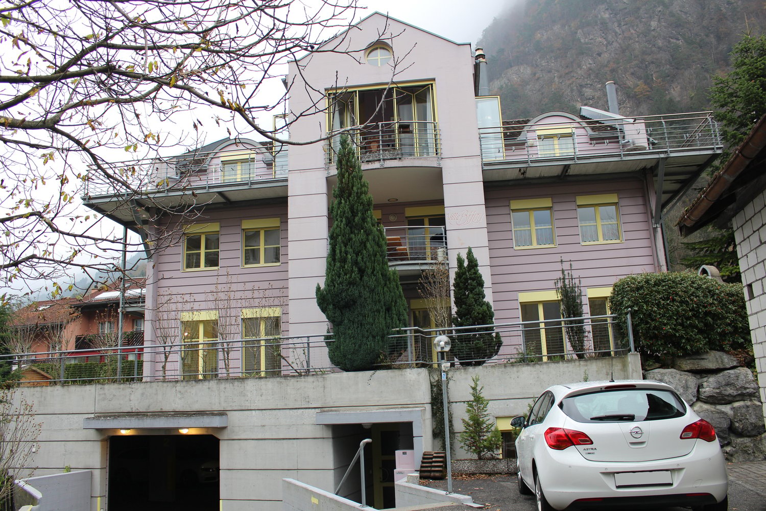 3 story house, pink and yellow painted, ground floor parking, balcony
