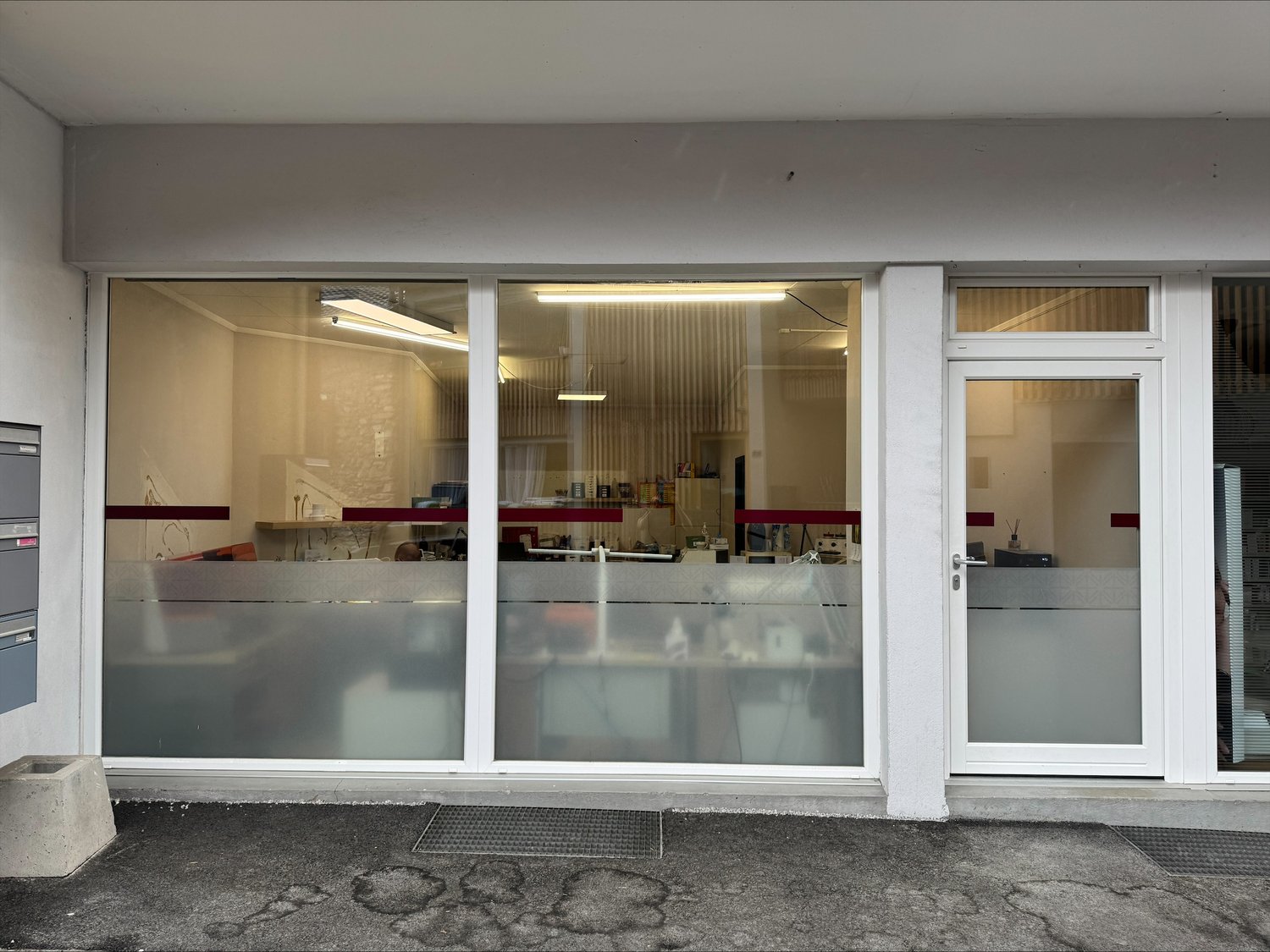 Commercial building with glass facade, white walls, two glass doors, and a small concrete planter.