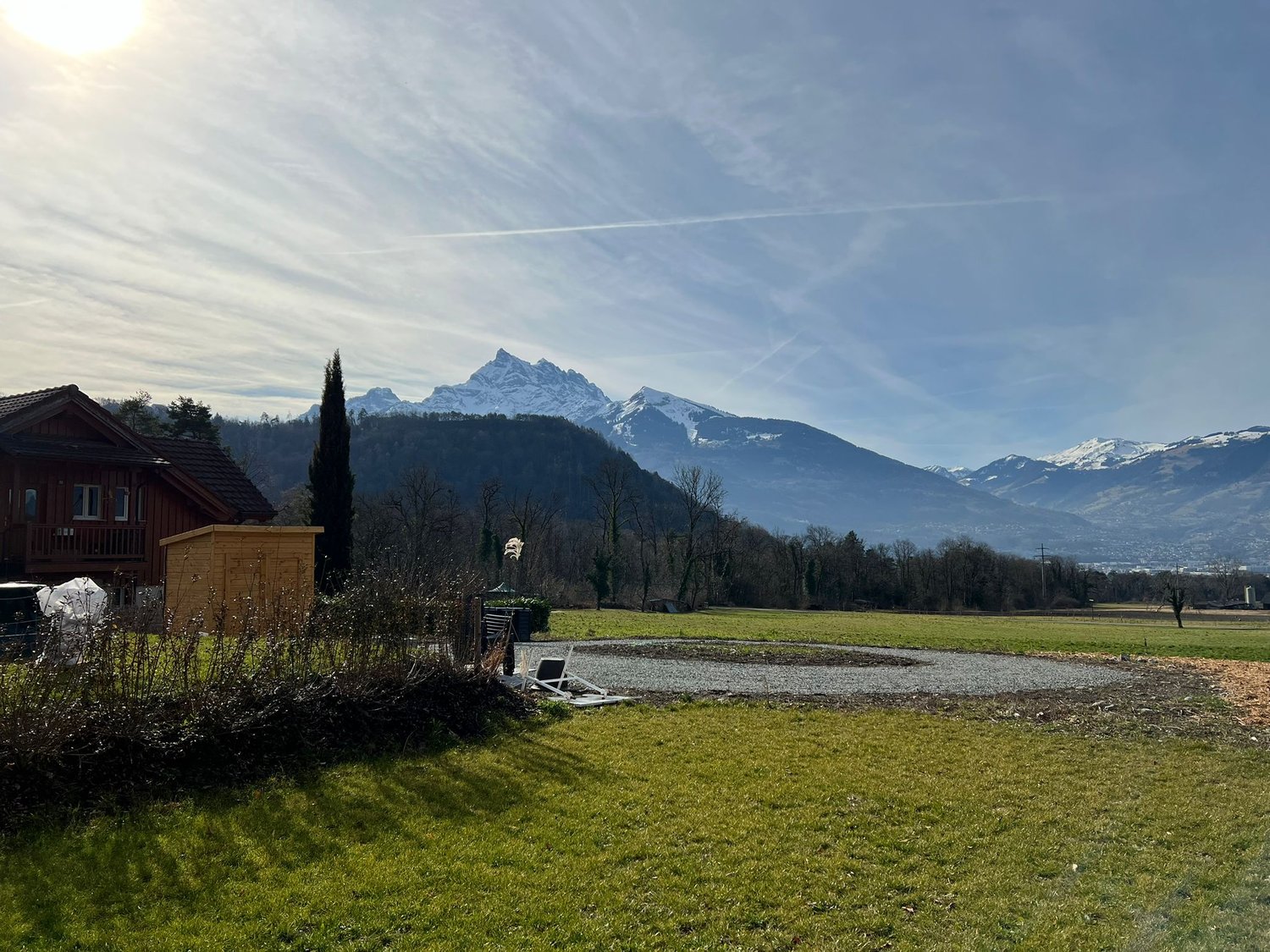 green grass, gravel path, wooden house, mountains in the background