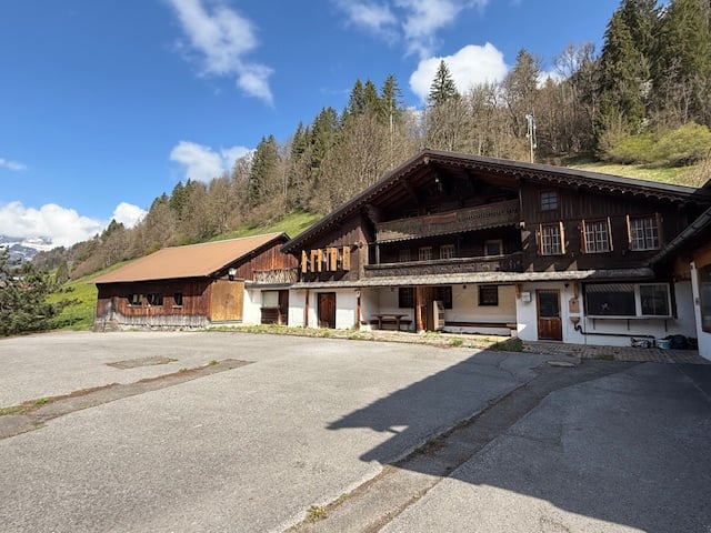 A large wooden chalet-style building with a parking area in front, surrounded by a forested mountain landscape.