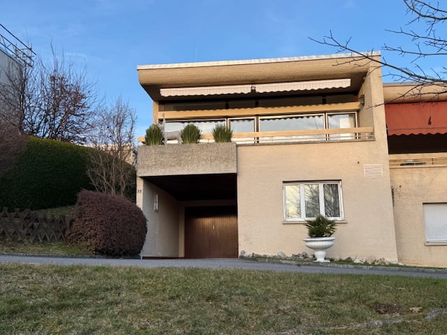 2 story building, raised ground floor, beige exterior, balcony, wooden door, large window, white planter