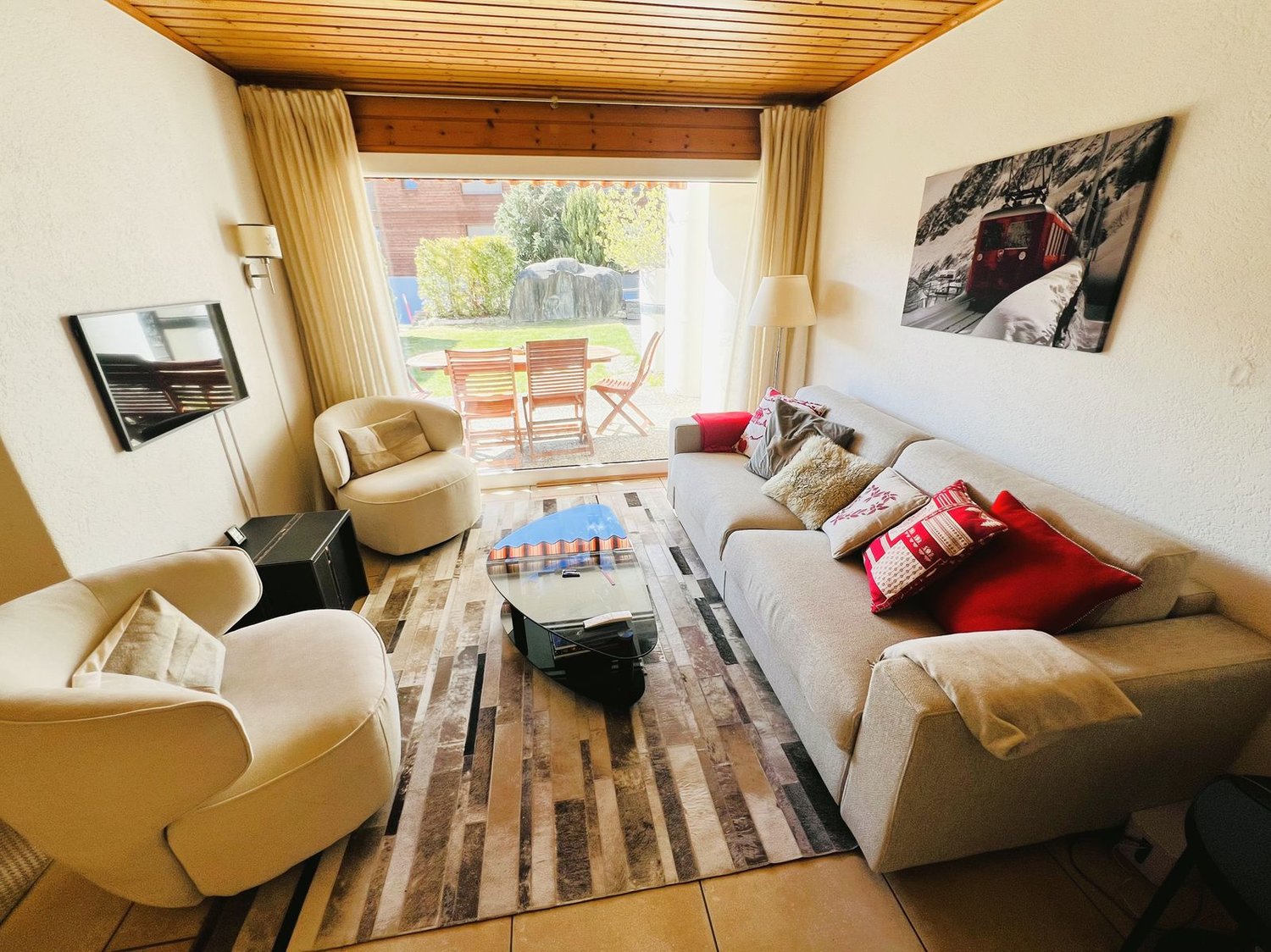large sofa, coffee table, armchairs, TV, rug, glass door to terrace