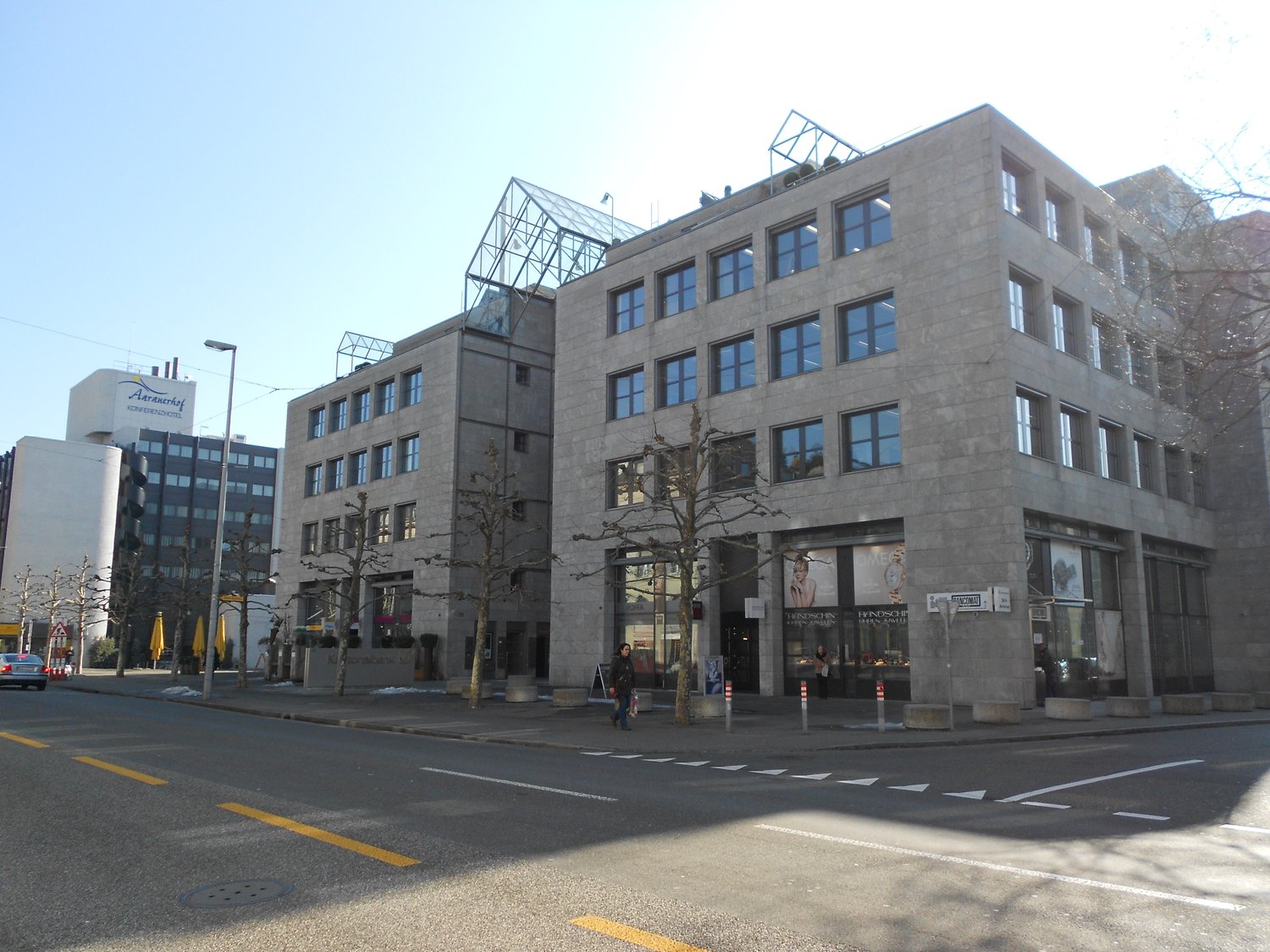 Commercial building, glass windows, grey walls, multiple floors, people walking, street lights, parked car