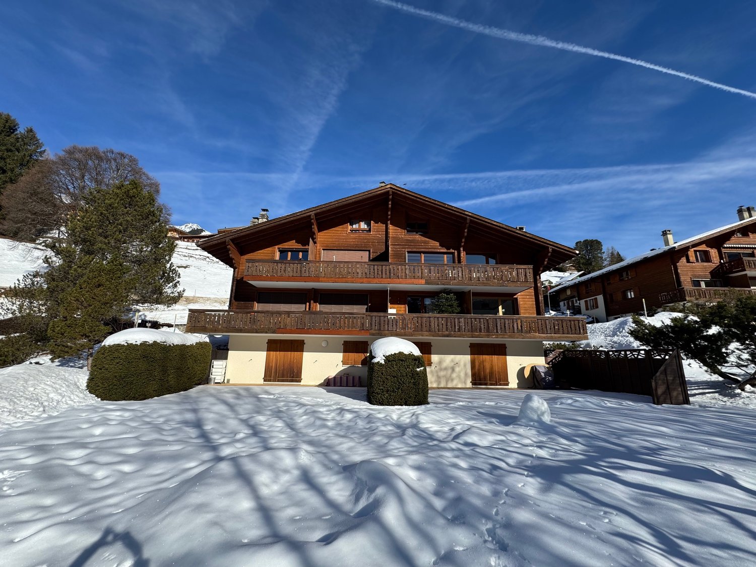 wooden exterior, wooden balconies, snow on ground, nearby trees, slope behind
