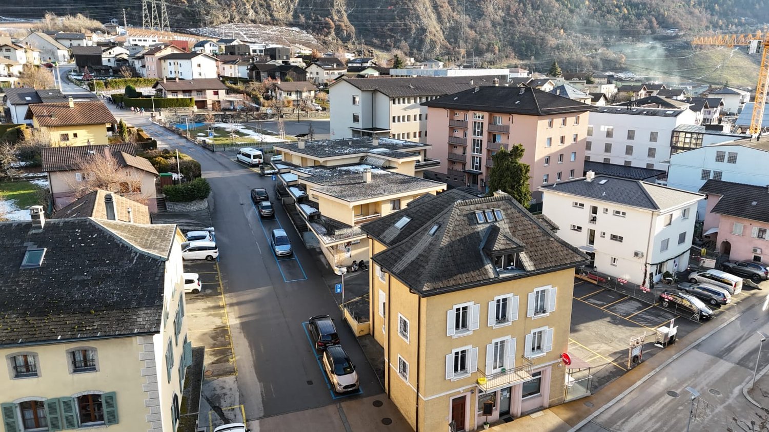 aerial view, neighborhood, residential buildings, cars parked on both sides of the road, multiple stories, some balconies