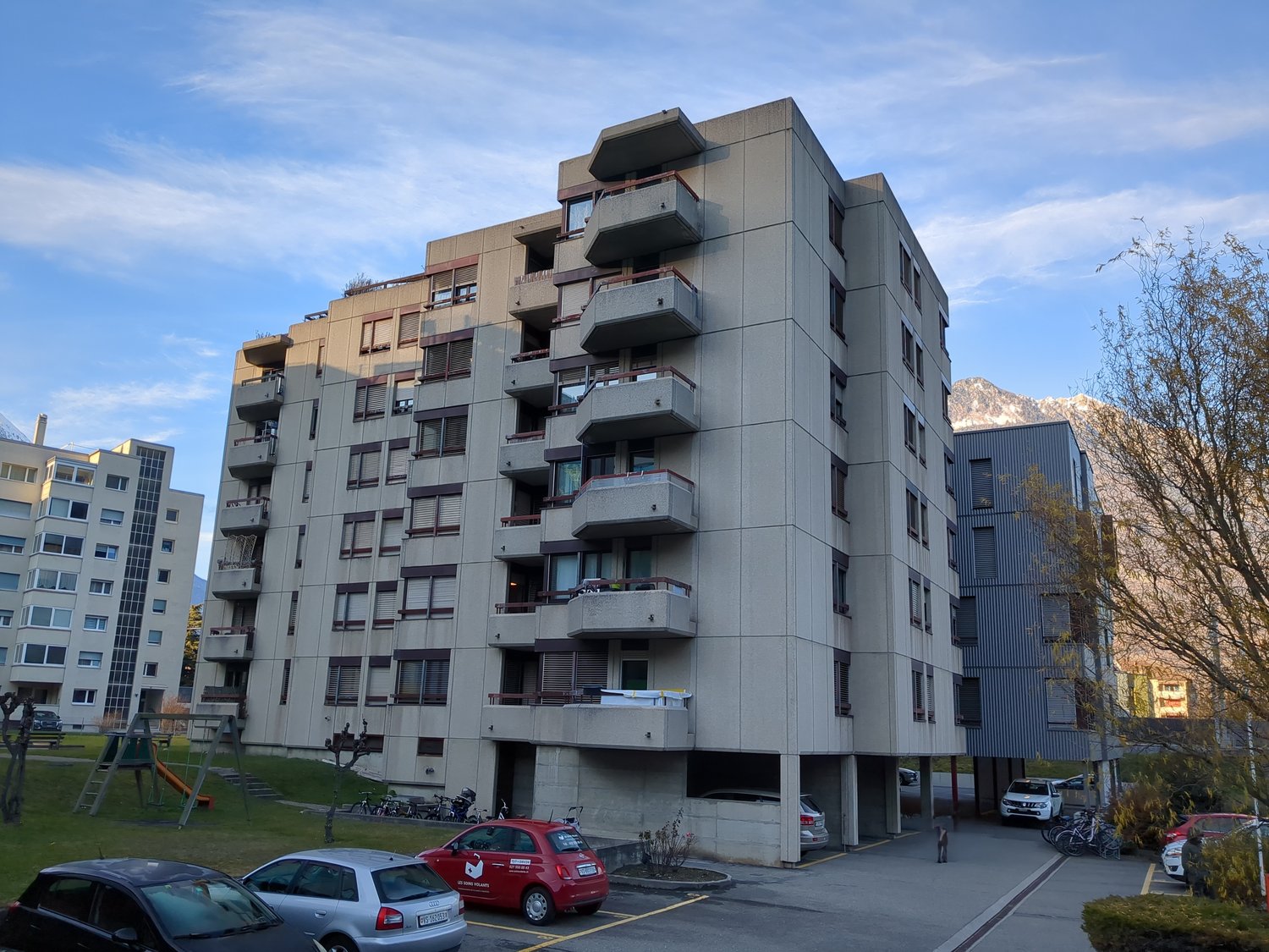 Multi-story apartment building with balconies, underground parking, multiple balconies, nearby playground, street view