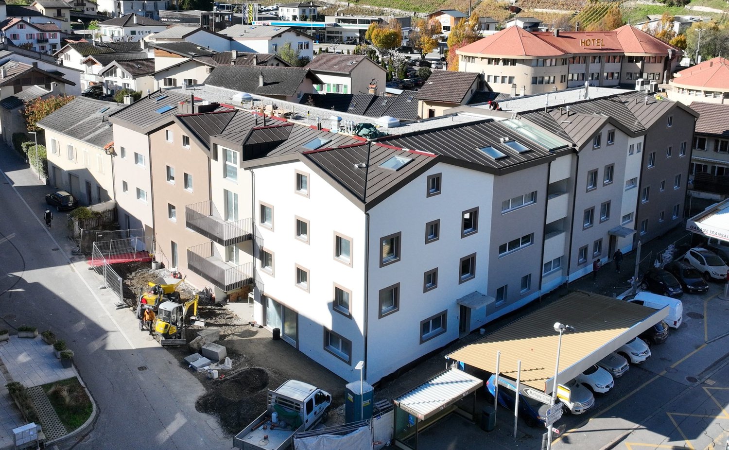 5 story building, white walls, brown roof, multiple windows, balconies, a car park, a hotel building, cars parked in front