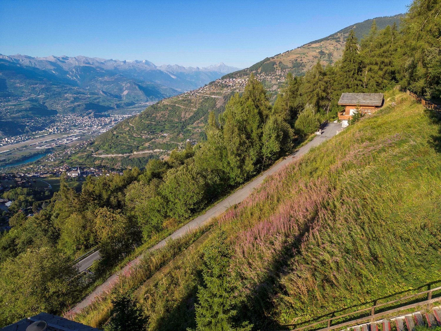 A small chalet on a hill with view of valley and mountains.