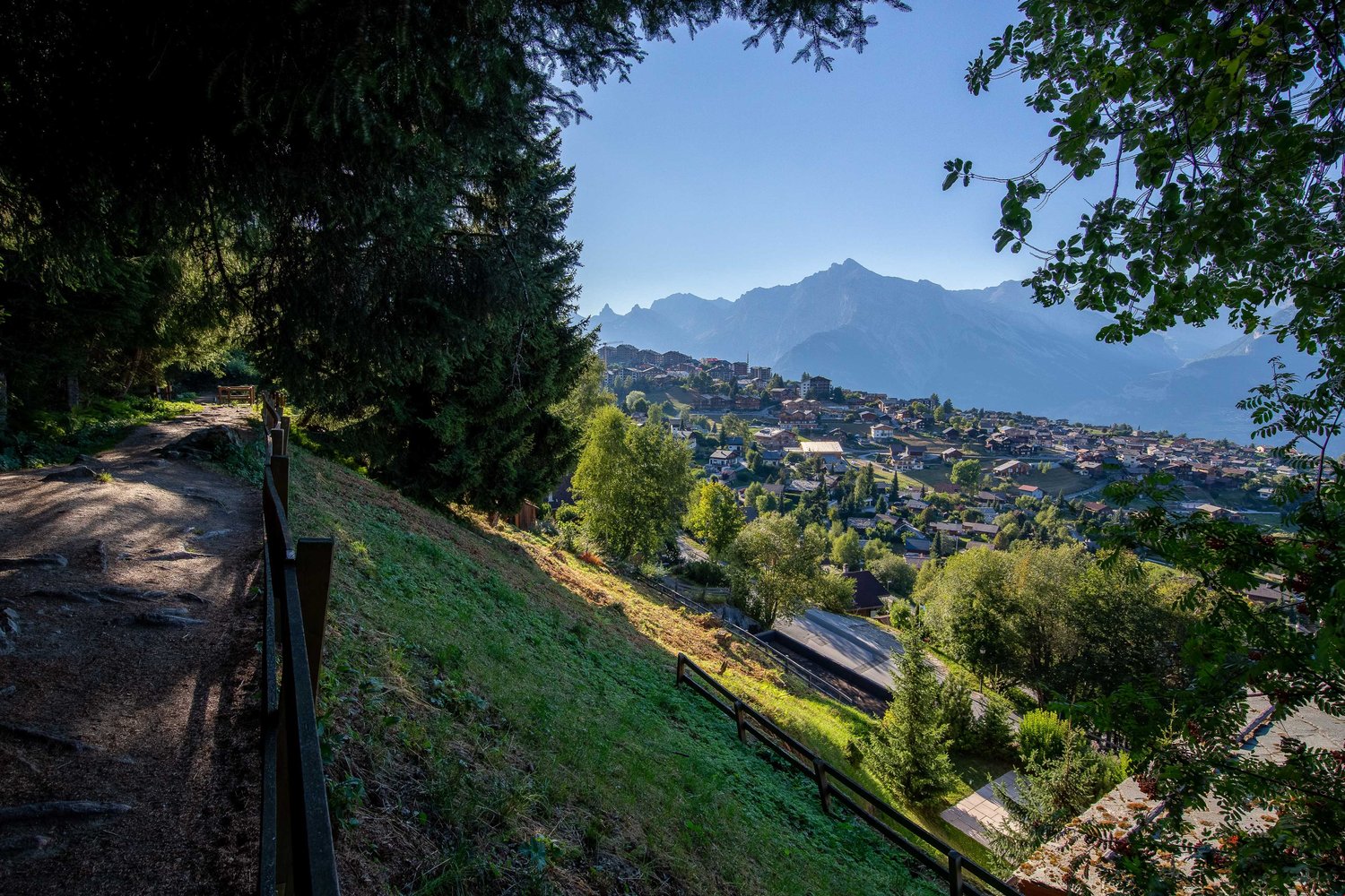 hillside path, grassy area, trees, village houses, mountains in background