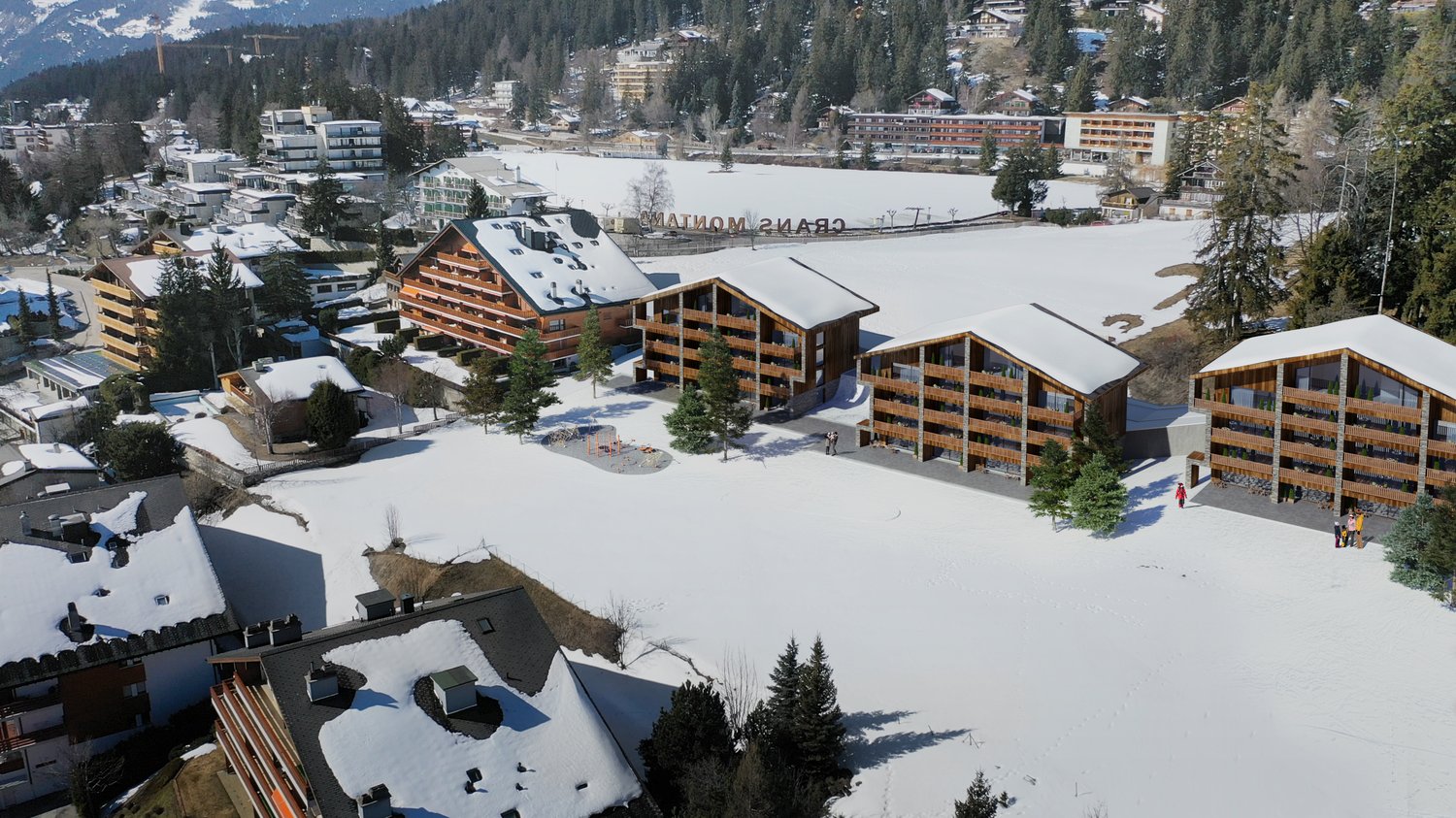 Building complex with multiple apartment buildings with snow on the ground and surrounding mountains.