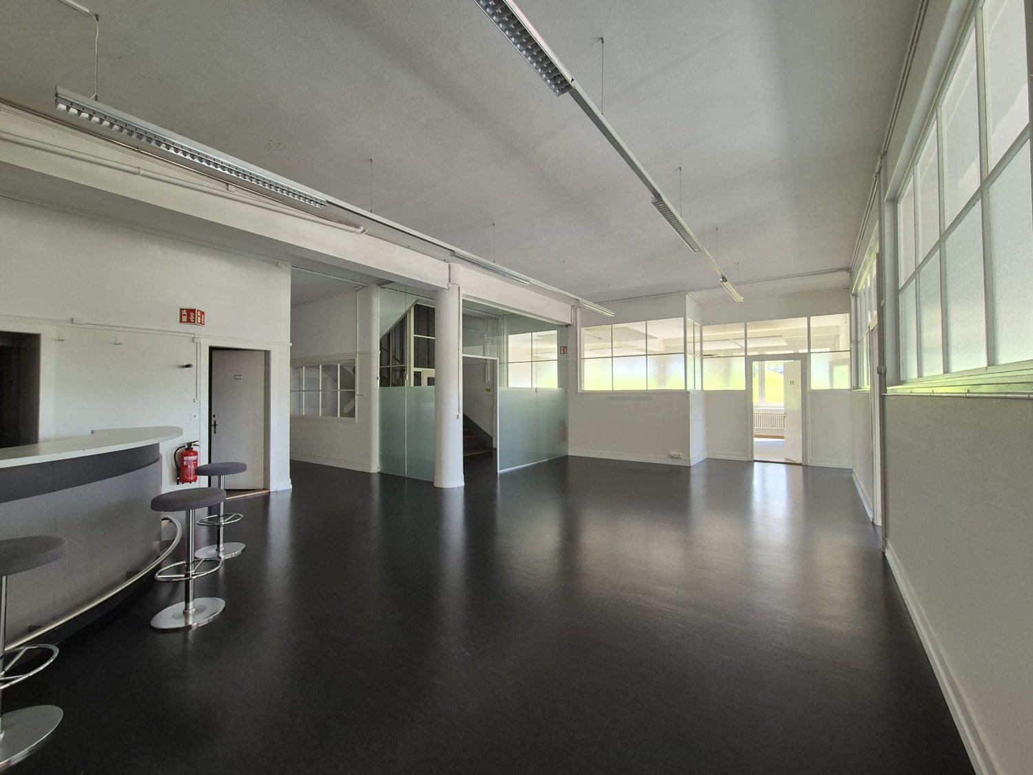 empty room with black floor, three stools, fire extinguisher, large windows, white walls