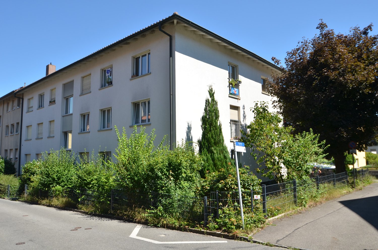 3 story white building, multiple windows, fenced garden, street sign